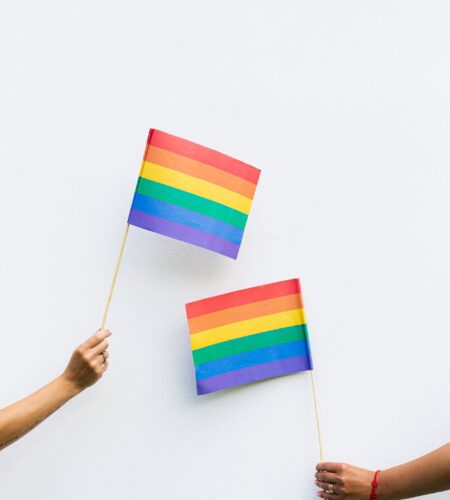 Zwei Hände halten jeweils eine bunte Regenbogenflagge